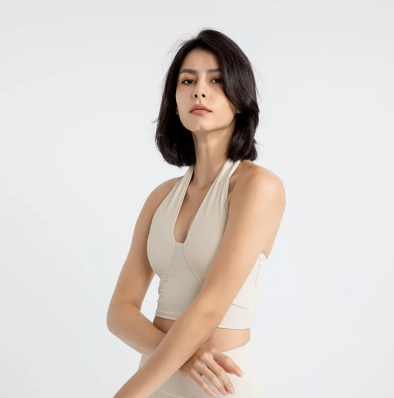 Woman in a beige sports bra with halter neckline and backless design, standing against a white background
